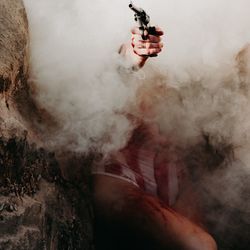 Midsection of mid adult woman holding handgun amidst smoke