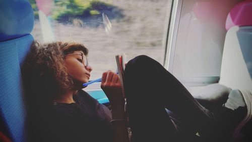 Side view of young woman writing on train