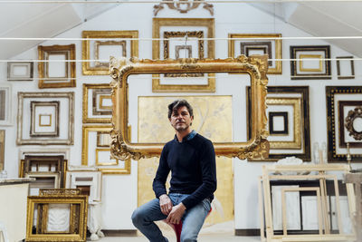 Mature man sitting on chair with frames in background