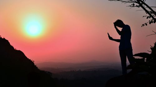 Silhouette man standing on mountain against sky at sunset