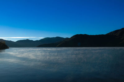 Scenic view of lake and mountains against clear blue sky