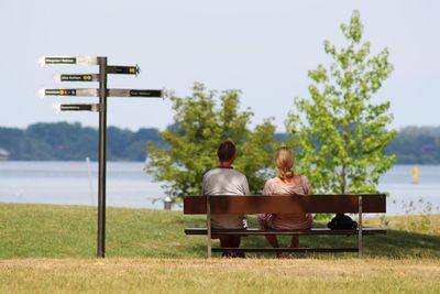 Rear view of couple sitting on bench against lake