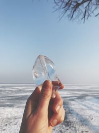 Close-up of hand holding crystal ball on beach against sky