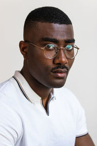 Confident adult african american guy in casual outfit and eyeglasses looking at camera on white background in light studio
