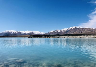 Scenic view of lake and snowcapped mountains against blue sky