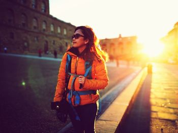 Young woman standing in city against sky during sunset