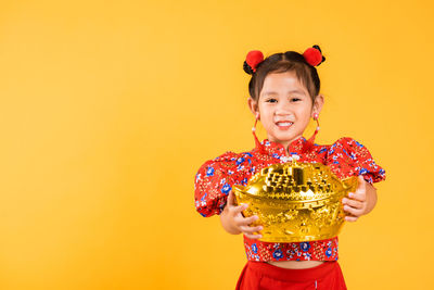 Portrait of smiling young woman standing against yellow background