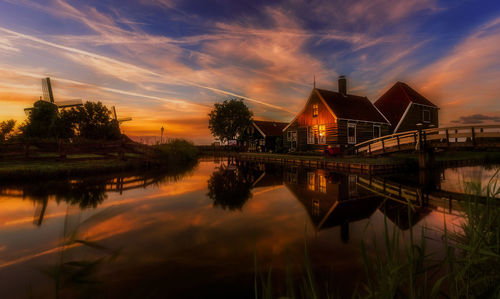 River by illuminated buildings against sky at sunset