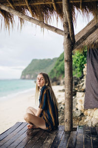 Young woman sitting on wood against sky