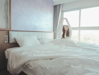 Asian young woman stretching morning wake up in bedroom on bed with white curtain background.