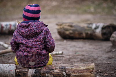 Rear view of girl sitting on wood in forest