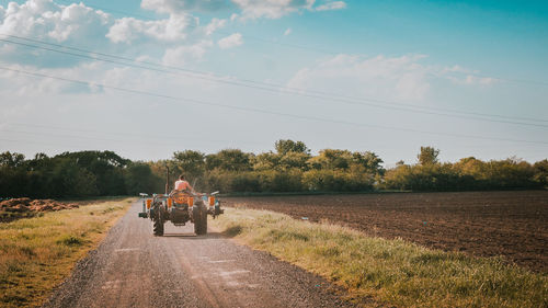 Rear view of man driving tractor on road against sky