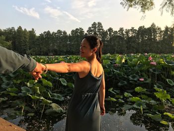 Cropped hand of man holding woman hands against lotus water lilies