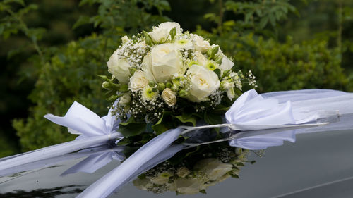 Bridal bouquet of white roses on the hood of a limousine