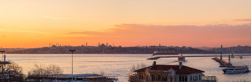 Panoramic view of buildings by sea against sky during sunset