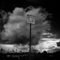 Low angle view of sign board against cloudy sky