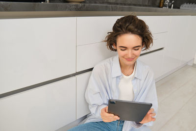 Portrait of smiling young woman using digital tablet while sitting at home