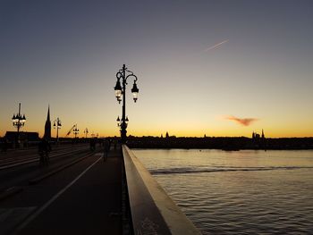 Street by silhouette city against sky during sunset