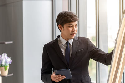Young businessman using digital tablet while writing on white board in office