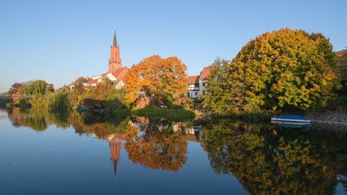 Trees by lake against sky during autumn