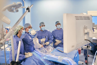 Surgeons in face mask and medical scrubs operating arthroscopic surgery while standing at operation room during covid-19