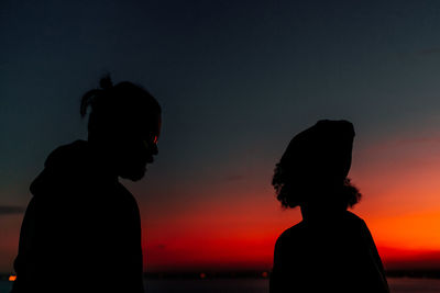Silhouette of couple standing at beach against clear sky during sunset