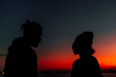 Silhouette couple standing at beach against clear sky during sunset