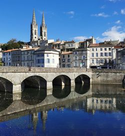 Arch bridge over river by buildings in city against blue sky