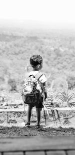 Rear view of boy standing on field against sky
