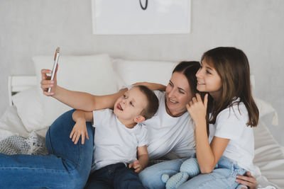 Happy mother taking selfie with kids on bed at home