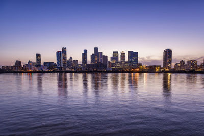 Sea by illuminated buildings against sky at dusk