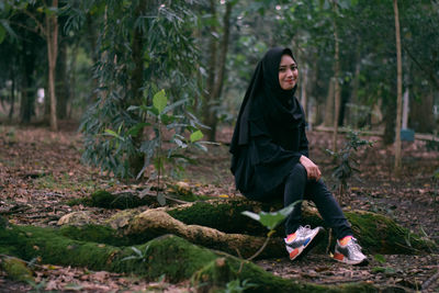 Portrait of young woman sitting on rock in forest