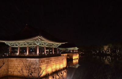 Illuminated building by lake against sky at night