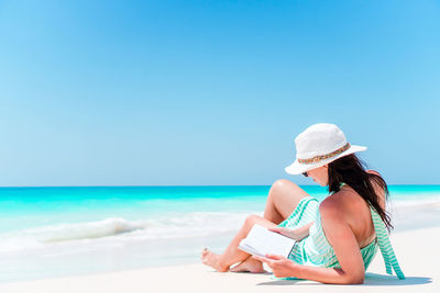 Woman with hat on beach against blue sky