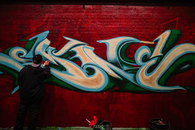 Rear view of man standing against graffiti wall