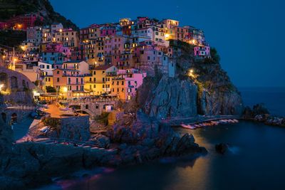 Illuminated townscape by sea against sky at dusk