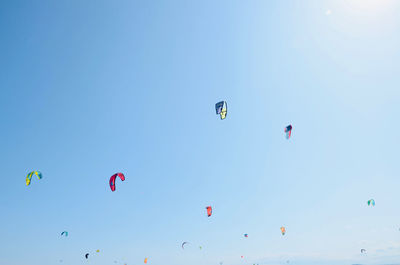 Low angle view of people paragliding against clear blue sky