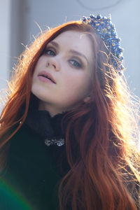 Beautiful red head girl with long hair in a crown of pearls stands on the street. high quality photo