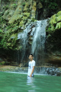 Portrait of young woman standing by waterfall in forest