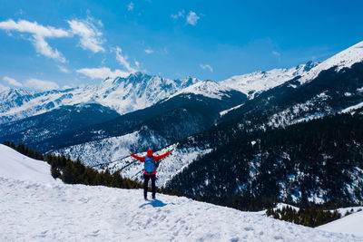 Rear view of man with arms outstretched standing on snowcapped mountain against sky