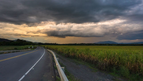 Road passing through field against cloudy sky