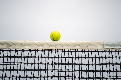 Close-up of tennis ball on net against sky