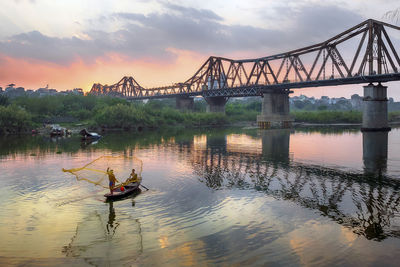 Two men fishing in river against sky during sunset