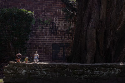 People sitting by tree trunk against brick wall