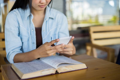 Midsection of woman using mobile phone while sitting on table