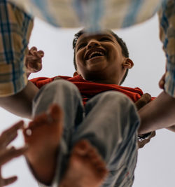 Low angle view of father holding cheerful son against clear sky