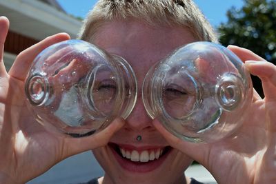 Close-up portrait of smiling boy holding glass bottles during summer