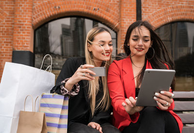 Young woman using smart phone while sitting on laptop