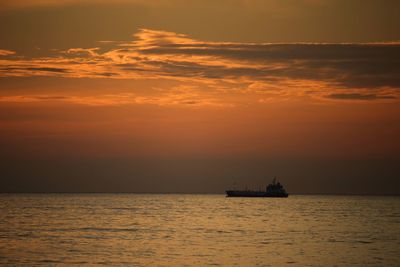 Silhouette boat in sea against cloudy orange sky during sunset