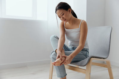 Young woman touching ankle pain sitting on chair